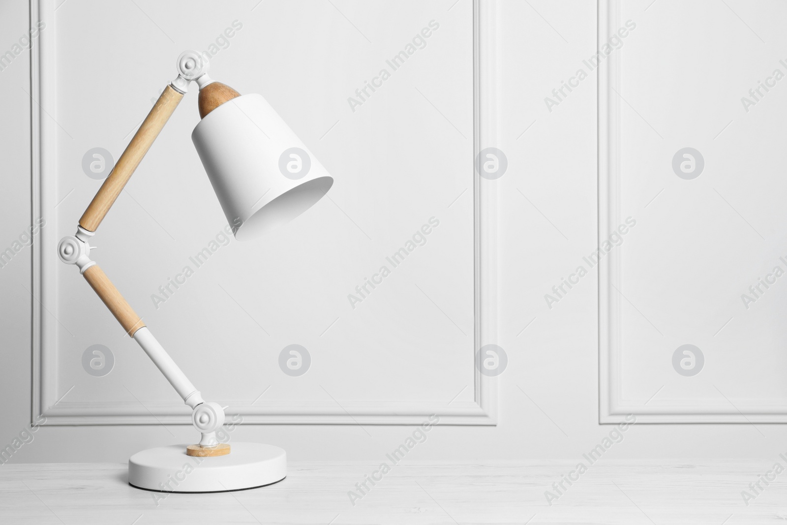 Photo of Stylish modern desk lamp on white wooden table, space for text