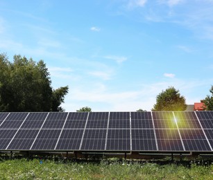 Solar panels near trees under blue sky on sunny day. Alternative energy source