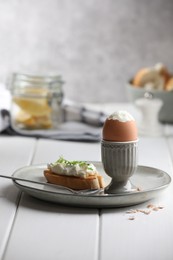 Photo of Fresh soft boiled egg in cup and sandwich on white wooden table