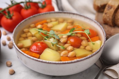 Photo of Tasty chickpea soup in bowl and ingredients served on white table, closeup