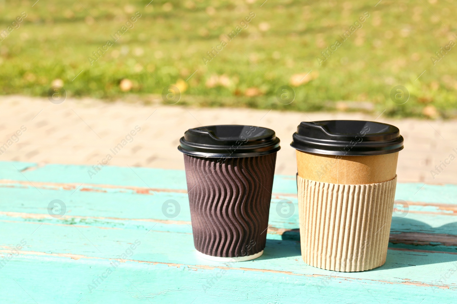Photo of Cardboard coffee cups on wooden table outdoors. Space for design