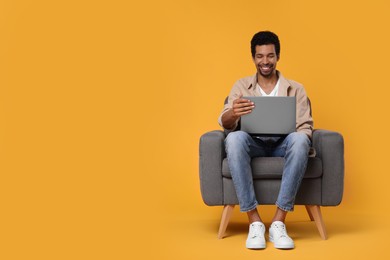 Photo of Happy man with laptop sitting in armchair on orange background. Space for text