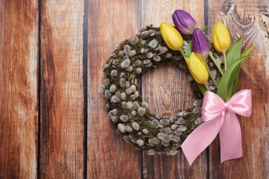Photo of Wreath made of beautiful willow, colorful tulip flowers and pink bow on wooden background, top view. Space for text