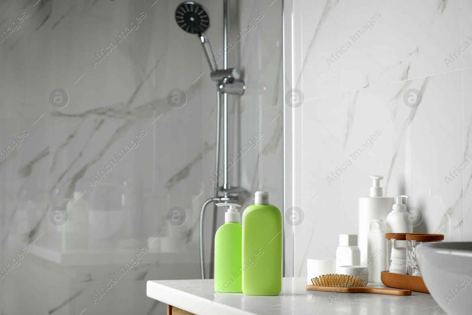 Photo of Shampoo, conditioner, other toiletries and wooden hairbrush on white table near shower stall in bathroom, space for text
