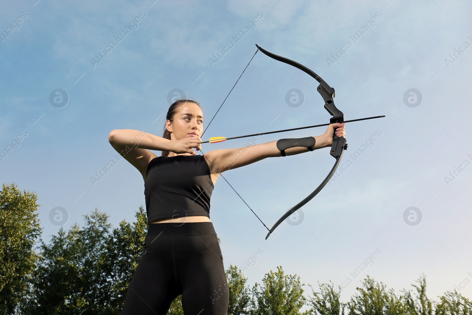 Photo of Woman with bow and arrow practicing archery outdoors, low angle view