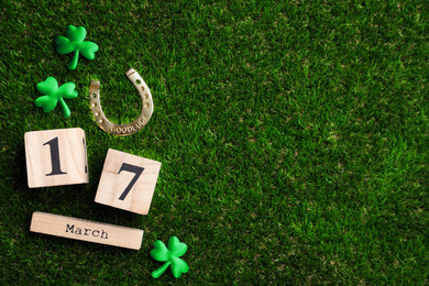Photo of Flat lay composition with horseshoe and wooden block calendar on grass, space for text. St. Patrick's Day celebration