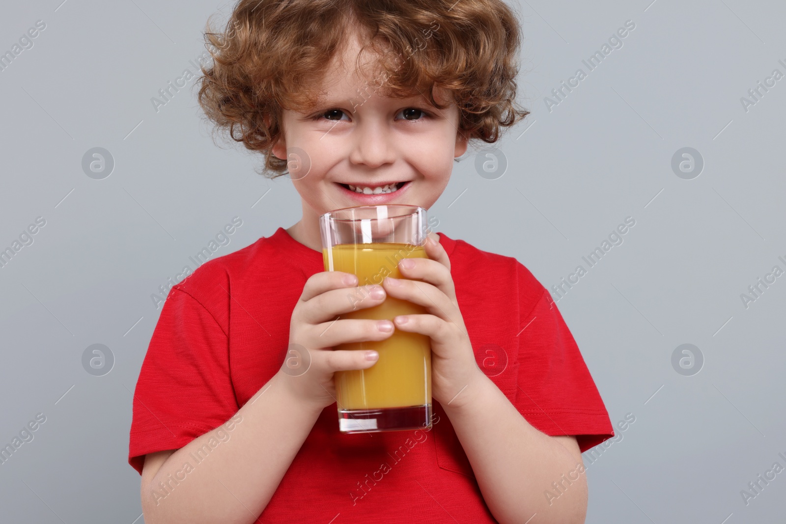 Photo of Cute little boy with glass of fresh juice on light gray background