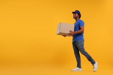 Photo of Happy courier with parcel on orange background, space for text