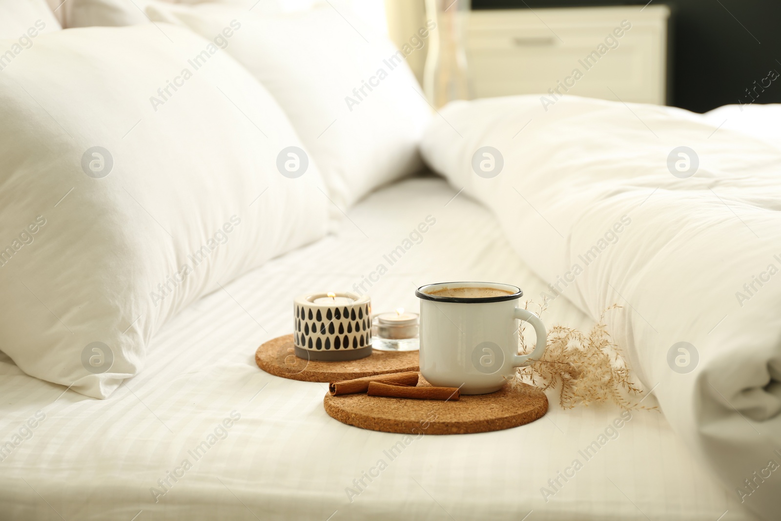 Photo of Cup of aromatic coffee and candle on bed with soft blanket