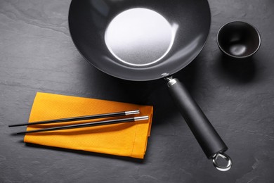 Photo of Empty iron wok, sauce bowl and chopsticks on black table