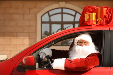 Authentic Santa Claus with bag full of presents on roof driving modern car, outdoors