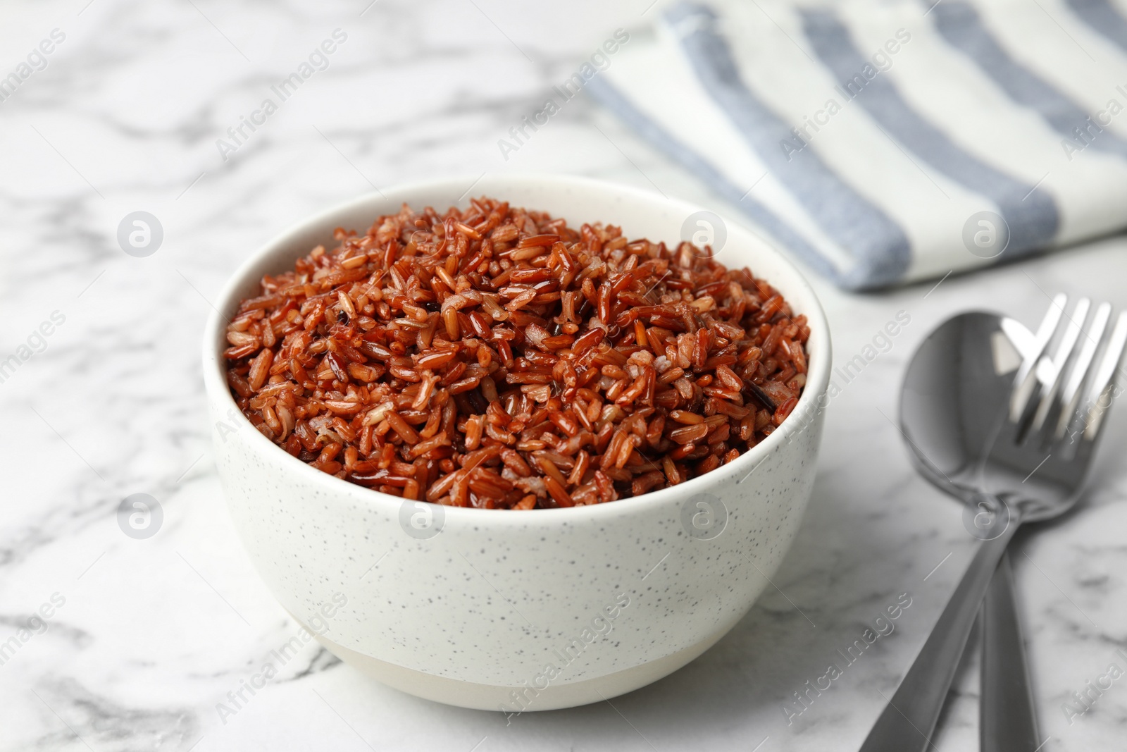 Photo of Bowl with delicious cooked brown rice on white marble table