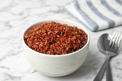 Bowl with delicious cooked brown rice on white marble table