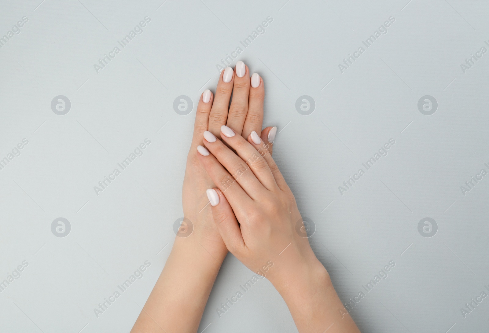 Photo of Woman with white polish on nails against light grey background, top view