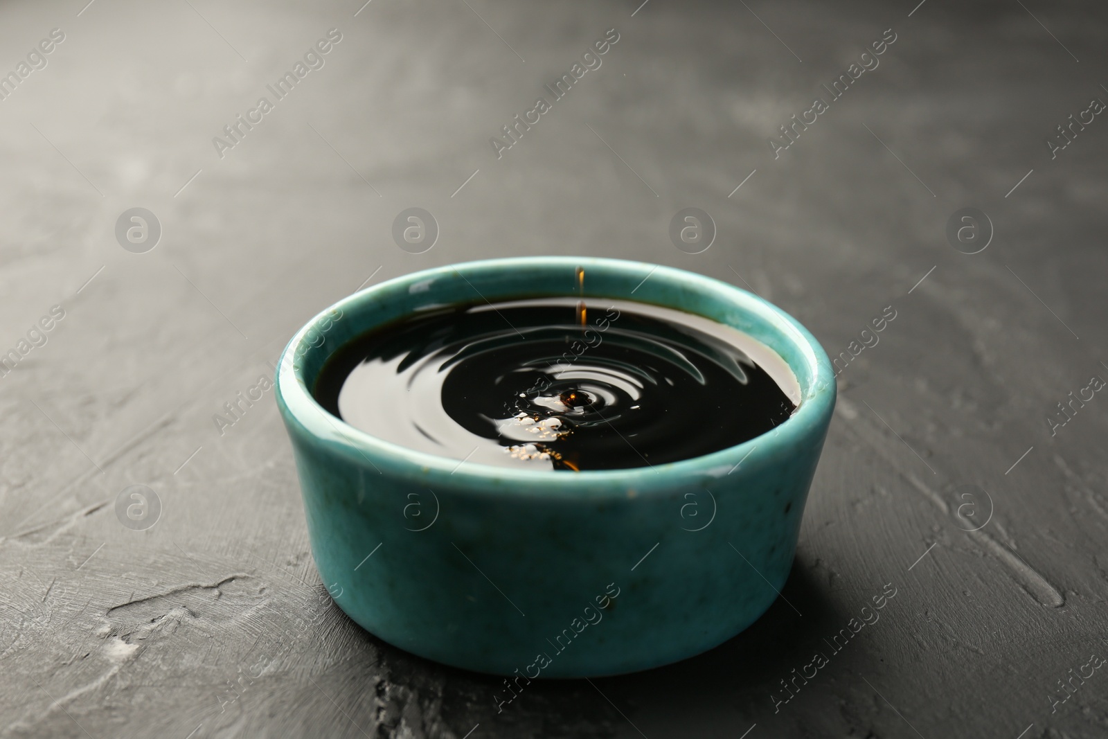 Photo of Tasty soy sauce in bowl on black table, closeup