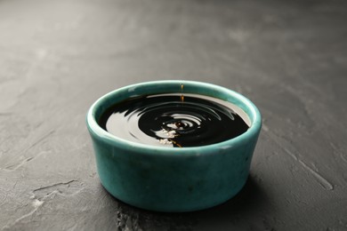 Tasty soy sauce in bowl on black table, closeup