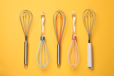 Photo of Different whisks on yellow background, flat lay