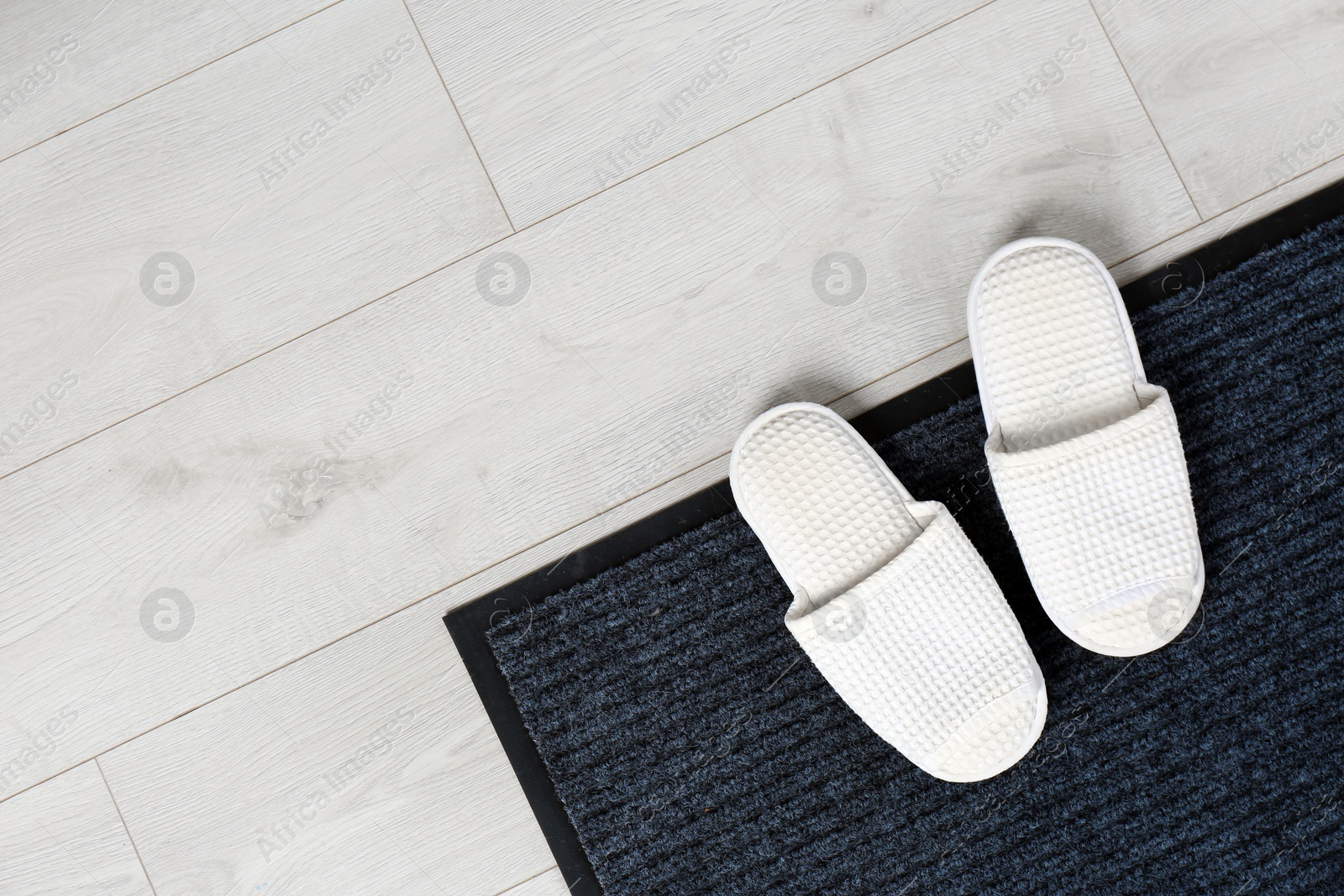 Photo of Door mat and slippers on floor, top view. Space for text