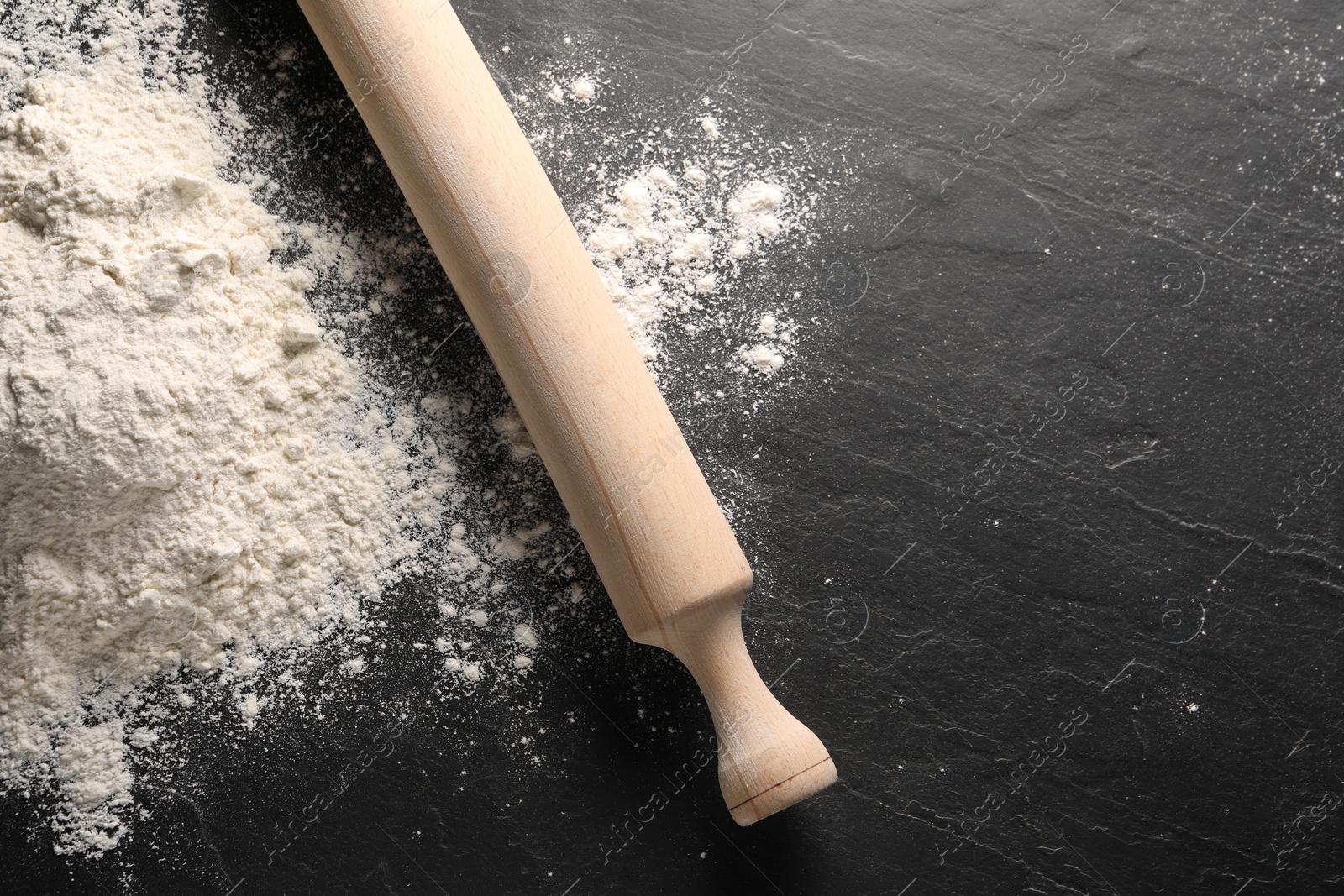 Photo of Pile of flour and rolling pin on black textured table, top view. Space for text