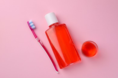 Fresh mouthwash in bottle, glass and toothbrush on pink background, flat lay