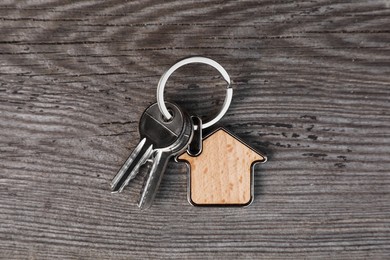 Keys with trinket in shape of house on wooden table, top view. Real estate agent services