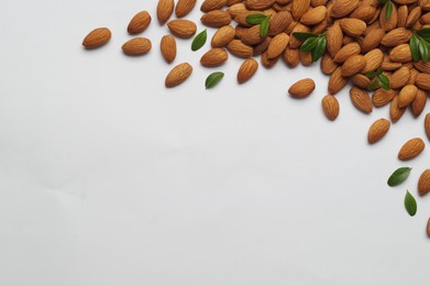 Delicious almonds and fresh leaves on white background, flat lay. Space for text