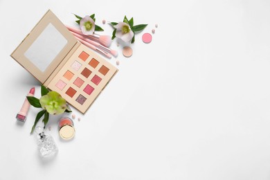 Flat lay composition with eyeshadow palette and beautiful flowers on white background, space for text