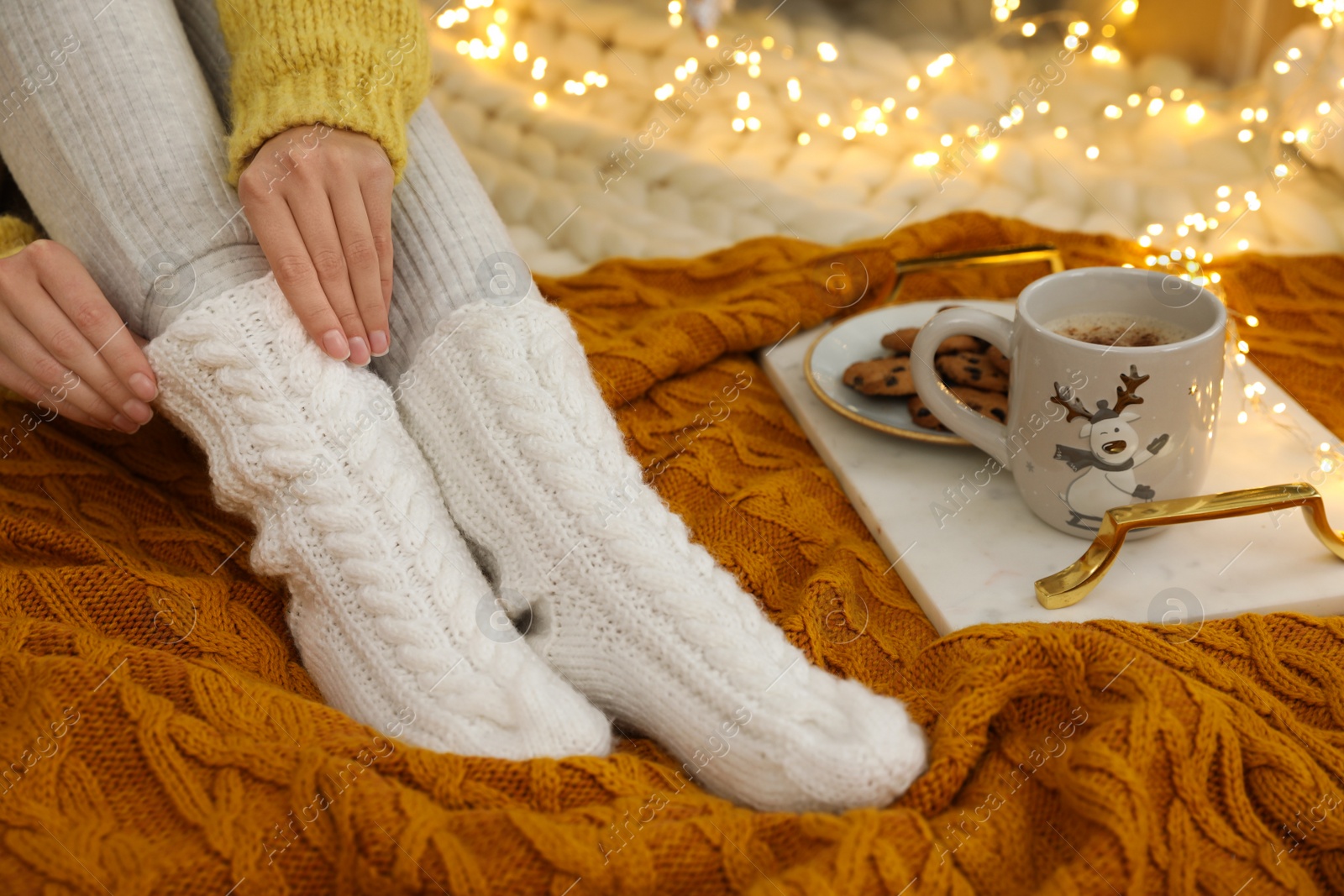 Photo of Woman in warm knitted socks sitting near tray with cup of hot drink and cookies on floor at home, closeup
