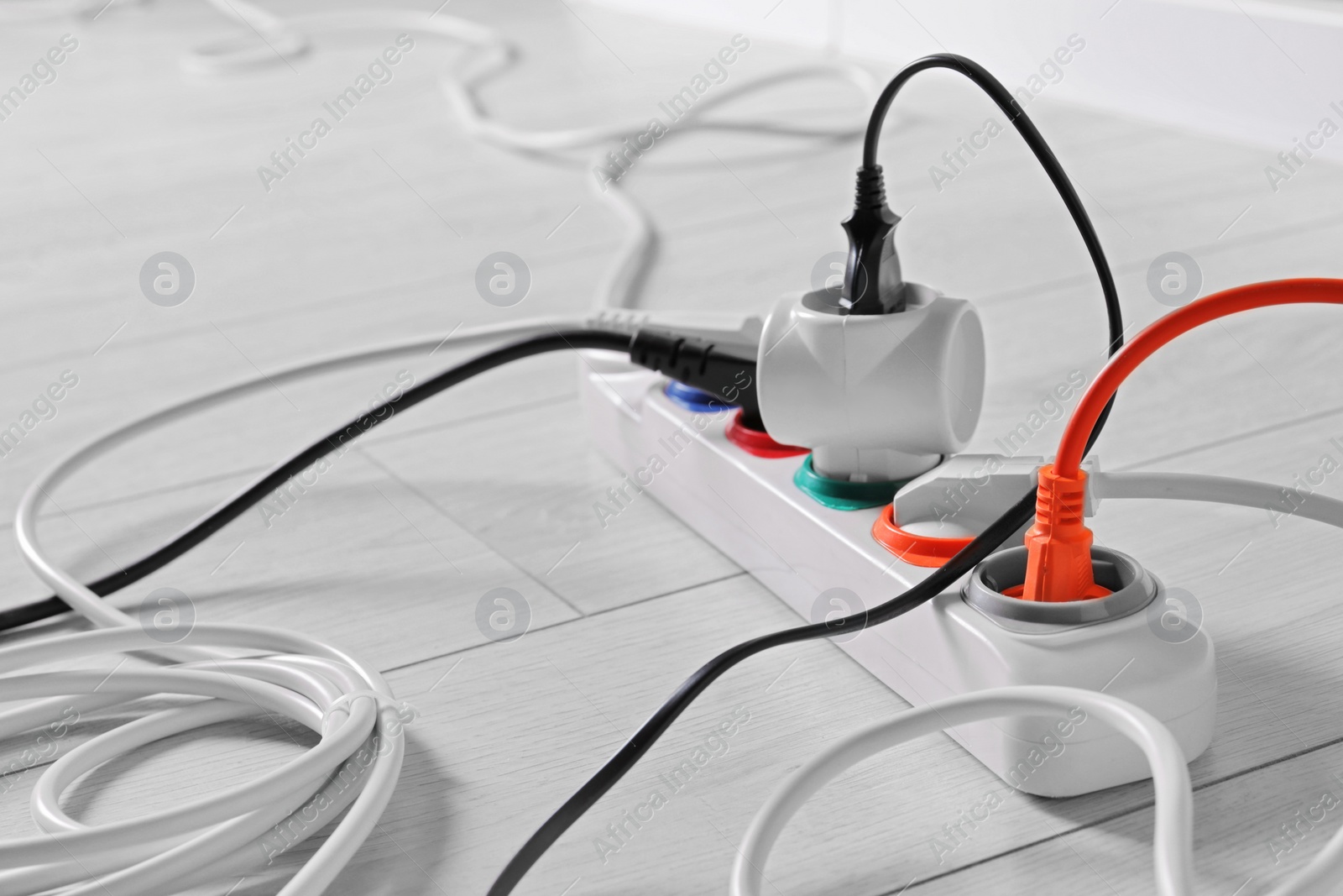 Photo of Power strip with different electrical plugs on white laminated floor, closeup