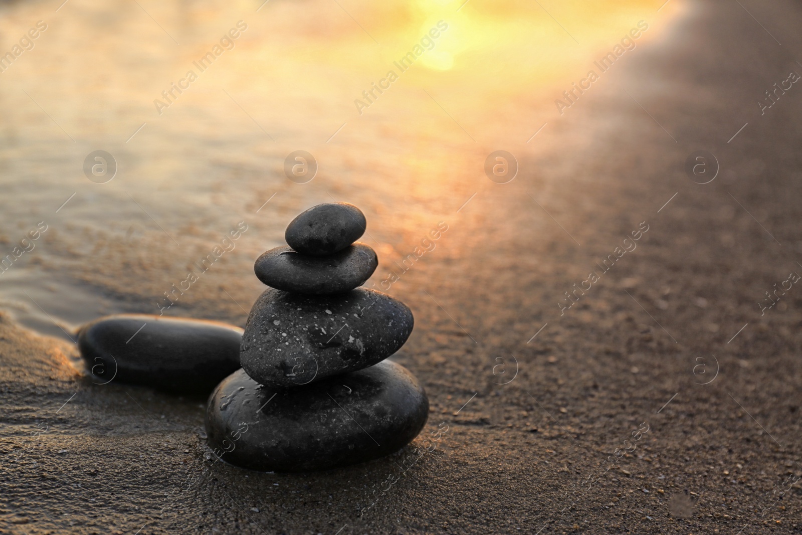 Photo of Dark stones on sand near sea at sunset, space for text. Zen concept