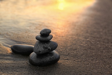 Photo of Dark stones on sand near sea at sunset, space for text. Zen concept