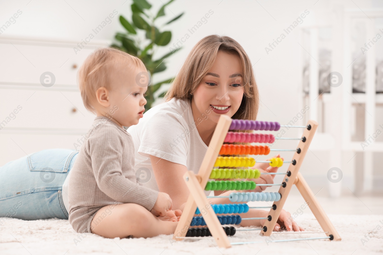 Photo of Children toys. Happy mother and her little son playing with wooden abacus on rug at home