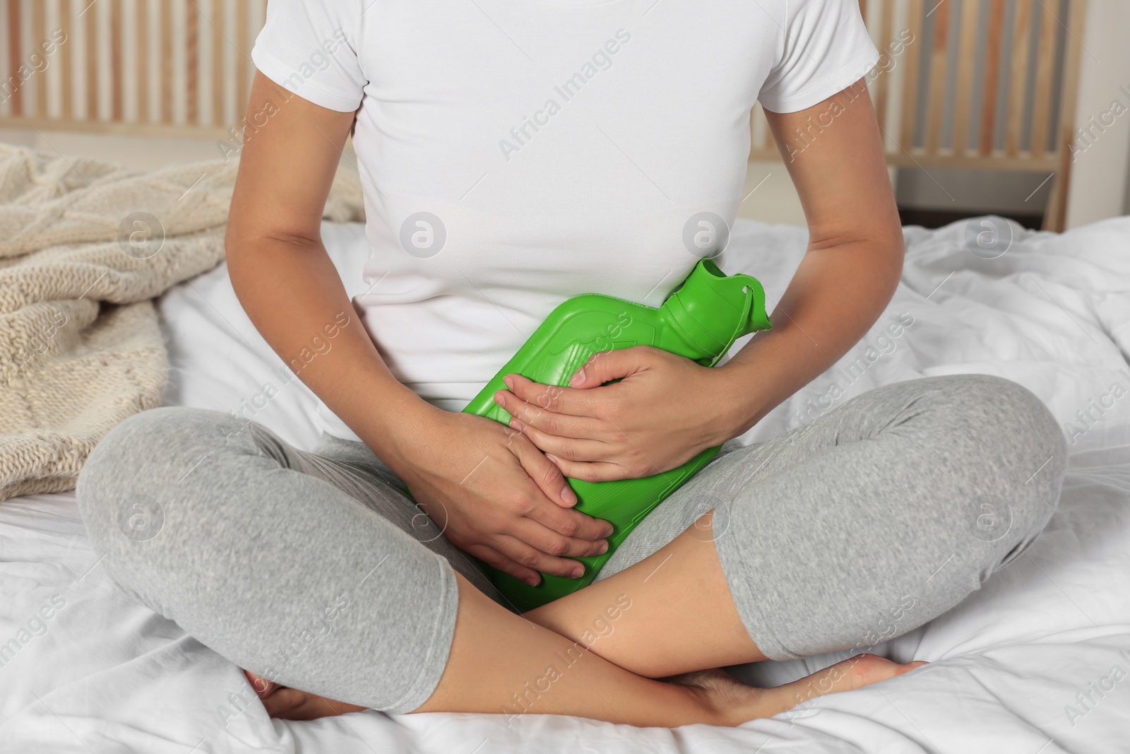 Photo of Young woman using hot water bottle to relieve cystitis pain on bed at home, closeup