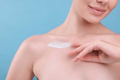 Woman with smear of body cream on her collarbone against light blue background, closeup