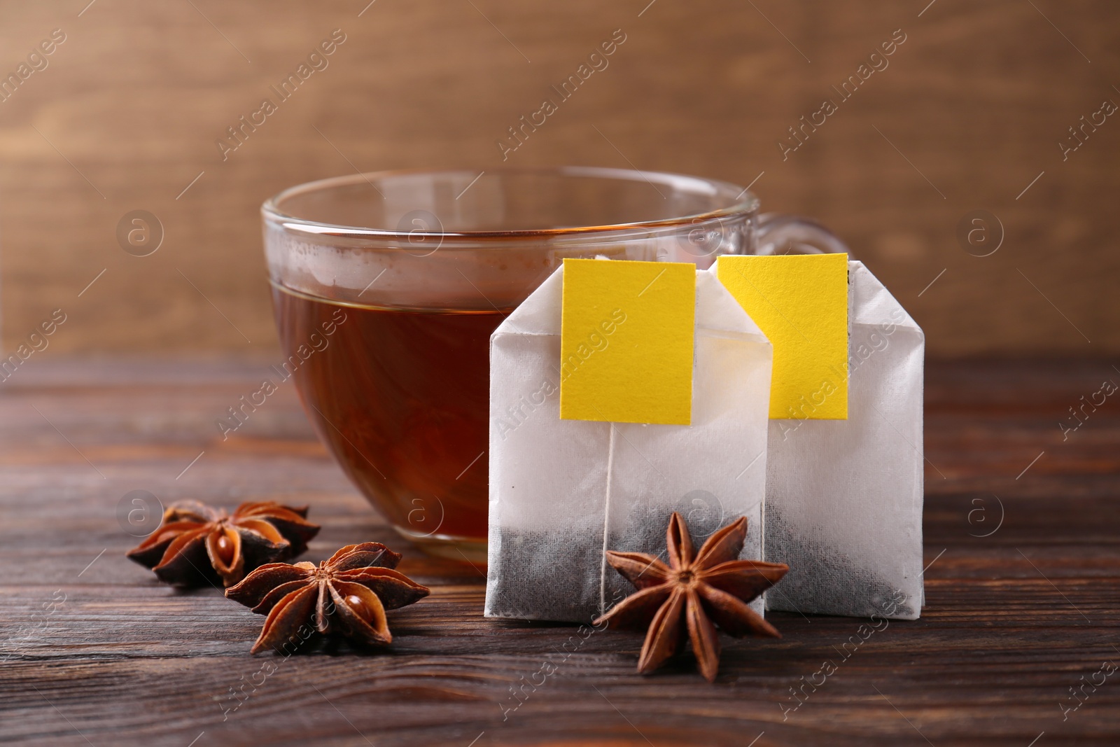 Photo of Tea bags, cup of hot drink and anise stars on wooden table, closeup