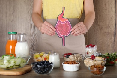 Woman holding paper intestine near table with food, closeup. Balanced nutrition for healthy digestive system