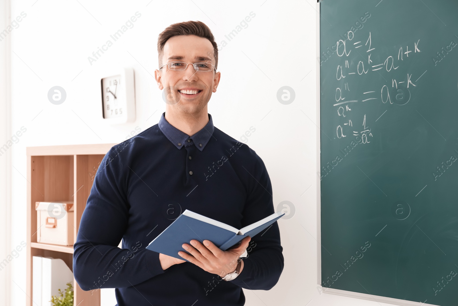 Photo of Young male teacher with book standing in classroom