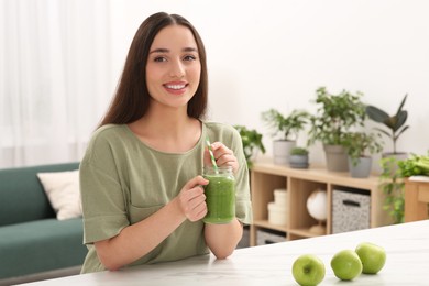 Photo of Beautiful young woman with mason jar of delicious smoothie and apples at home