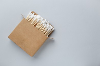 Photo of Cardboard box with cotton buds on light grey background, top view. Space for text