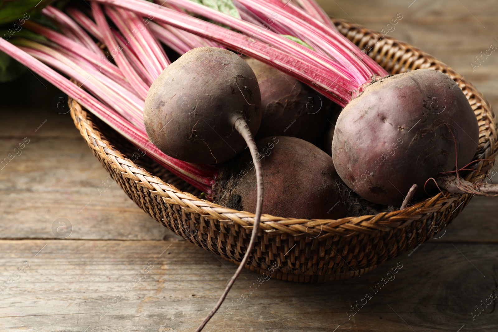 Photo of Raw ripe beets in wicker bowl on wooden table