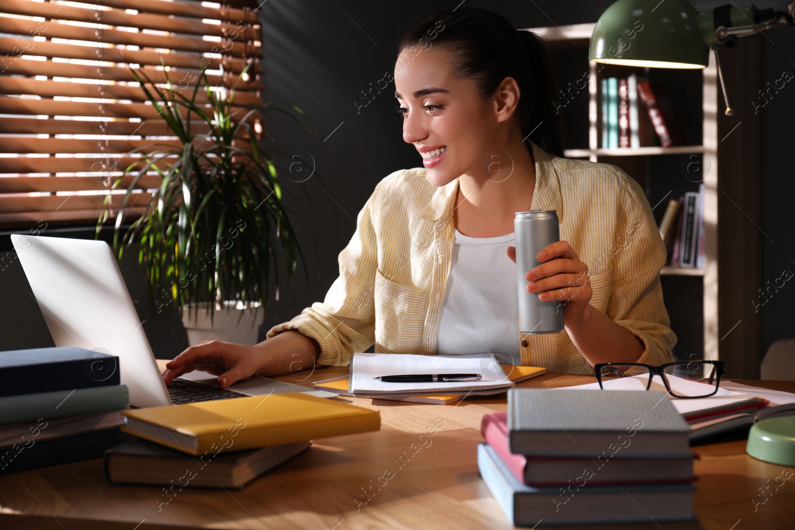 Photo of Young woman with energy drink studying at home