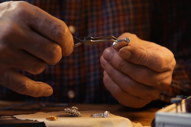 Photo of Professional jeweler working with ring at wooden table, closeup