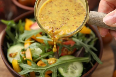 Woman pouring tasty vinegar based sauce (Vinaigrette) into bowl with salad at table, closeup