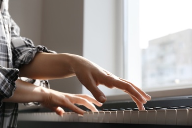 Young woman playing piano near window at home, closeup