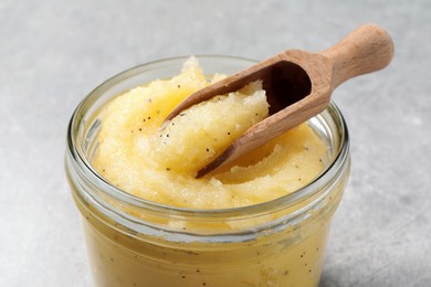 Photo of Body scrub with scoop in glass jar on light grey background, closeup
