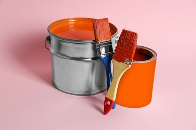 Photo of Bucket of orange paint, can and brushes on pink background