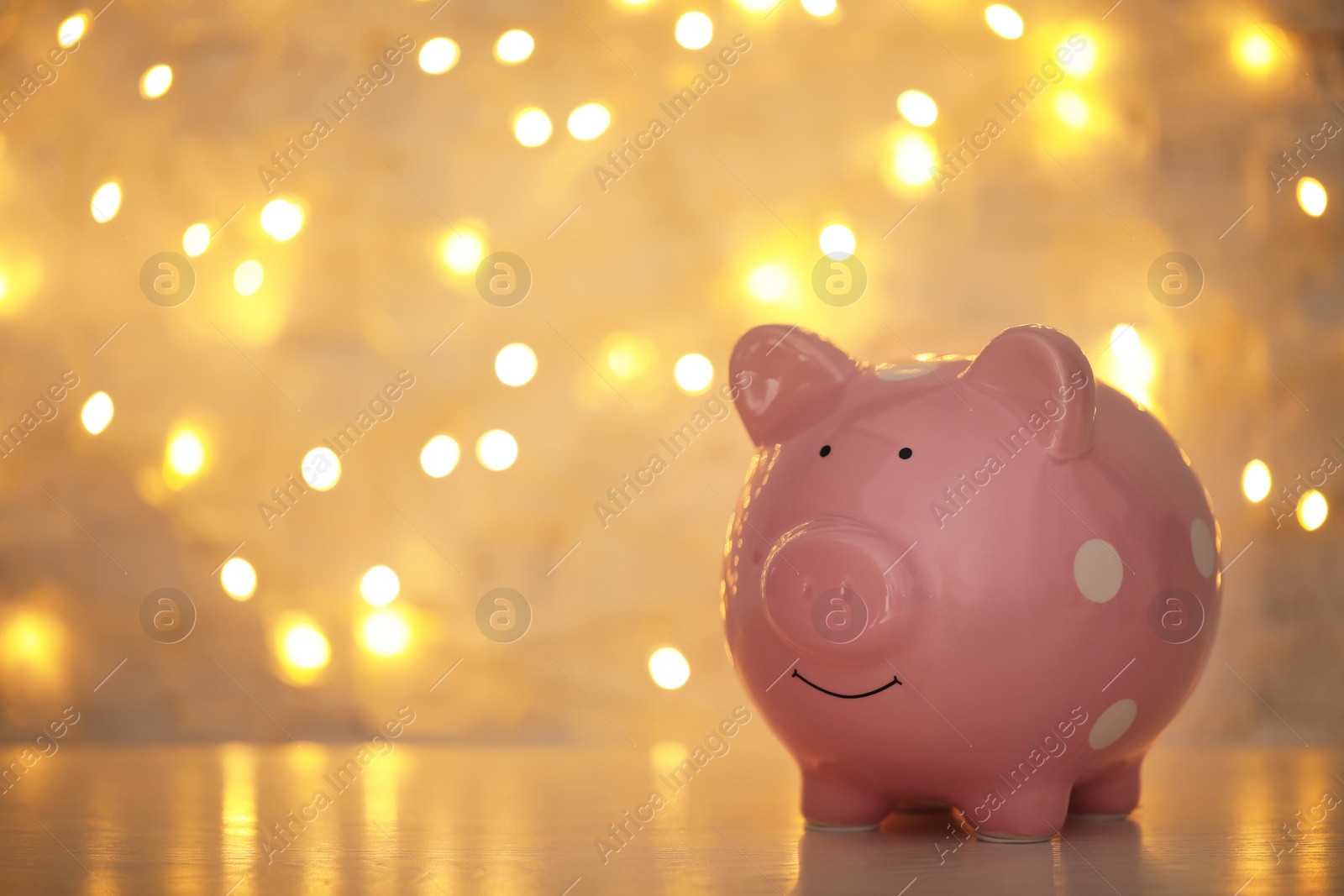 Photo of Piggy bank on wooden table against blurred Christmas lights, space for text