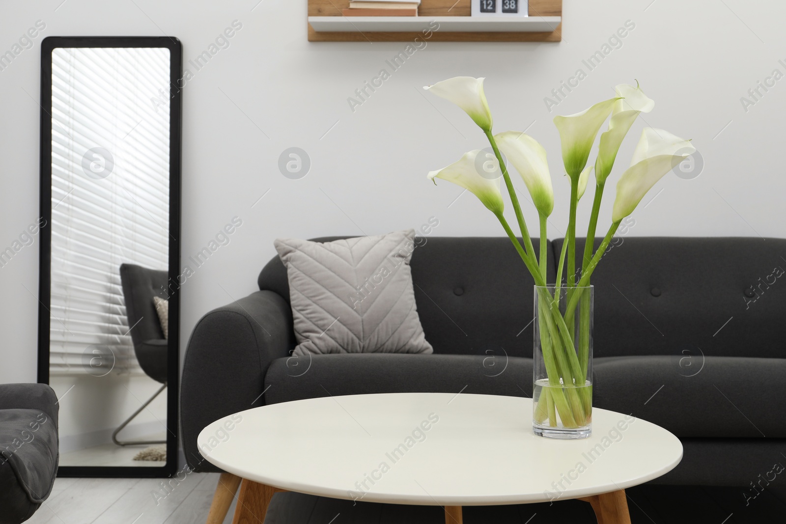 Photo of Beautiful calla lily flowers in glass vase on white table at home