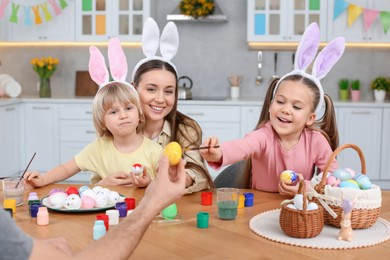 Happy family painting Easter eggs at table in kitchen