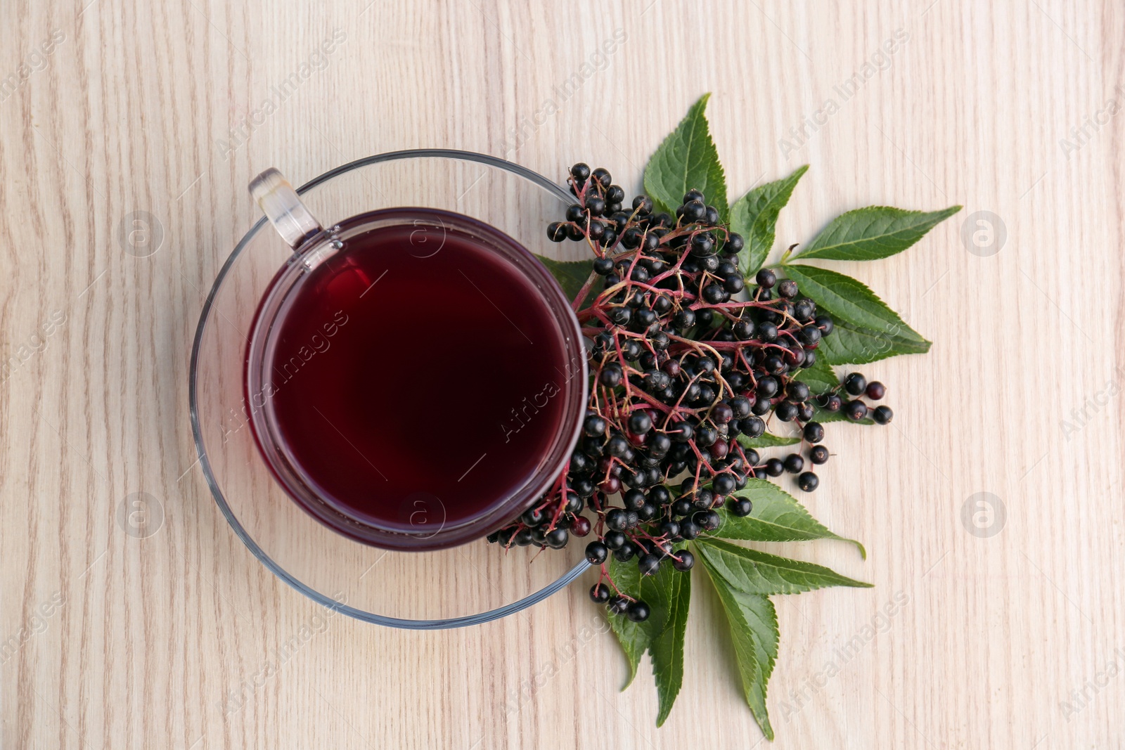 Photo of Glass cup of tasty elderberry tea and Sambucus berries on wooden table, top view